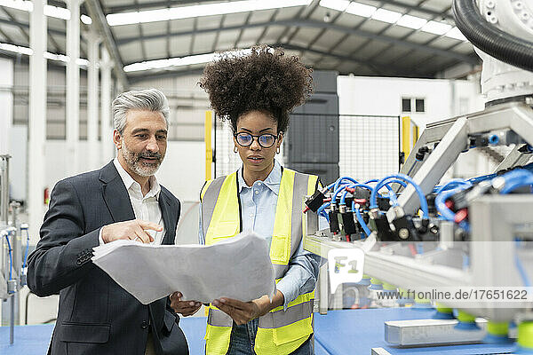Businessman discussing over blueprint with engineer in factory