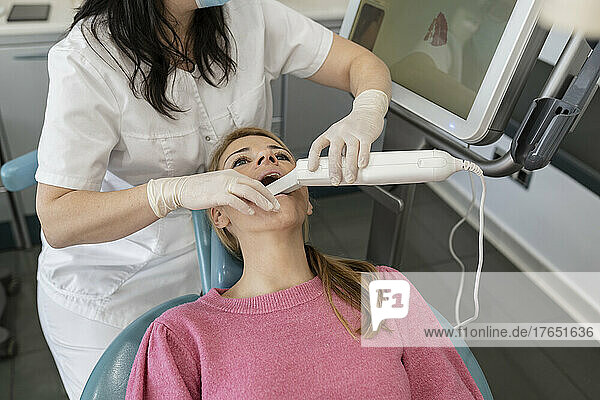 Dentist using dental camera for scanning teeth of patient at dental clinic