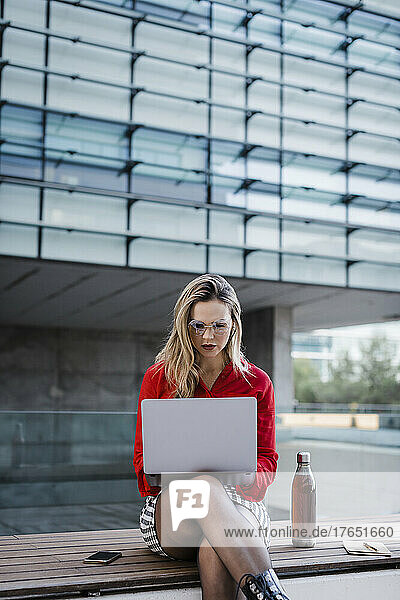 Businesswoman using laptop sitting on bench