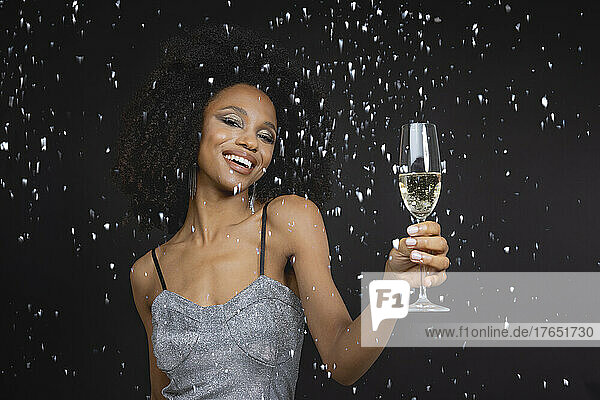 Glückliche junge Frau hält Champagnerglas vor schwarzem Hintergrund