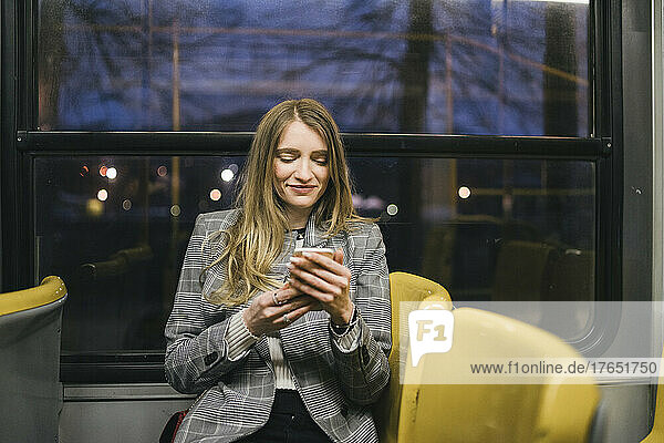Smiling woman using smart phone sitting in tram