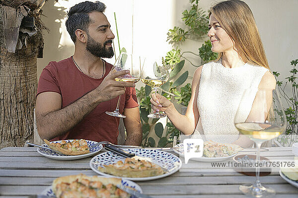 Couple toasting wineglasses sitting with savory pie in backyard