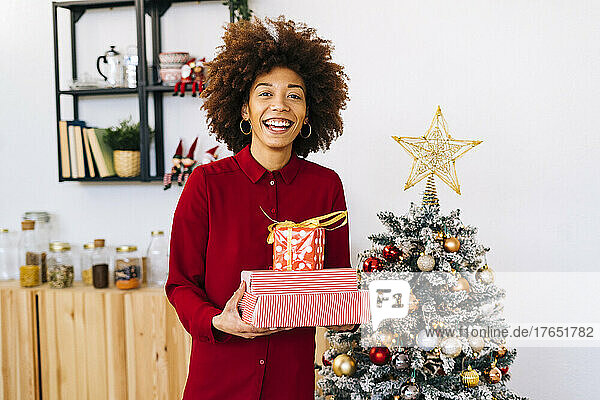 Glückliche Frau mit Geschenken  die zu Hause am Weihnachtsbaum steht