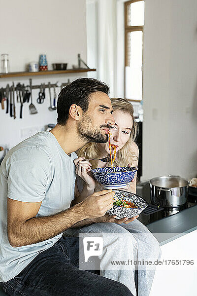 Boyfriend and girlfriend eating noodles in kitchen at home