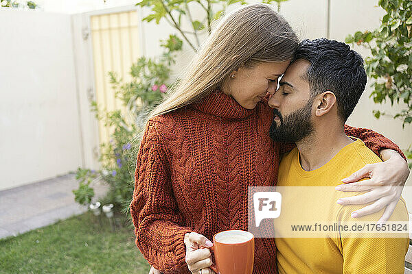 Frau mit Kaffeetasse sitzt mit Arm um Mann im Garten