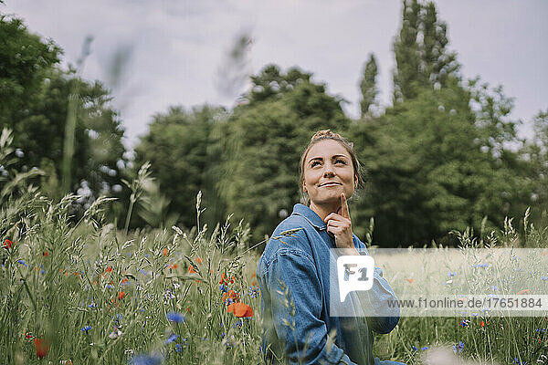 Contemplative woman with hand on chin amidst plants in meadow