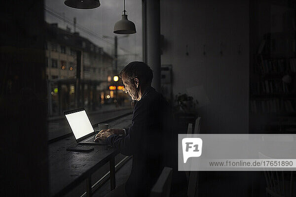 Businessman working on laptop in dark at cafe