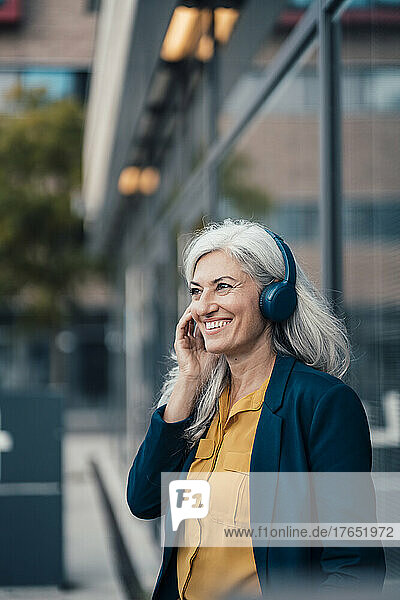 Happy businesswoman with gray hair enjoying music through wireless headphones