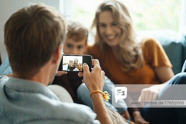 Man photographing woman and son through smart phone at home