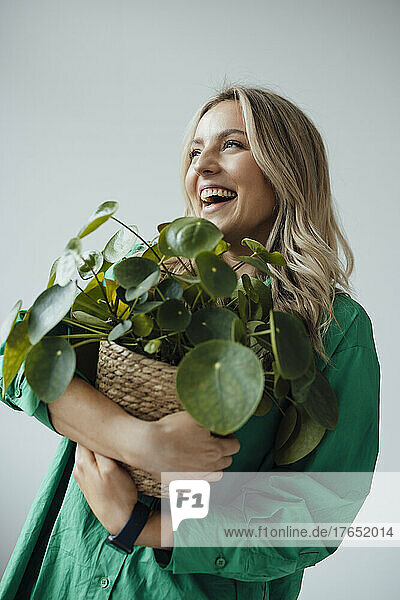 Cheerful woman holding houseplant against white background
