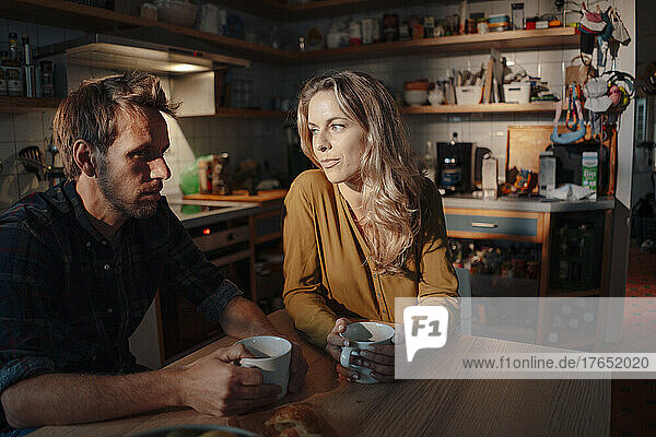 Man and woman with coffee cups sitting at table in kitchen