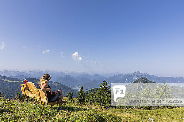 Germany  Bavaria  Female hiker relaxing on bench at summit of Fockenstein mountain