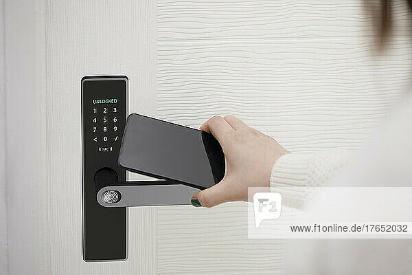 Woman unlocking smart door of house with mobile phone