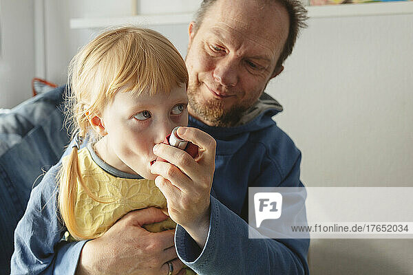 Father helping daughter using asthma inhaler at home