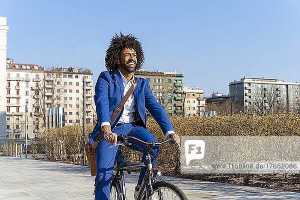 Happy businessman with shoulder bag sitting on bicycle