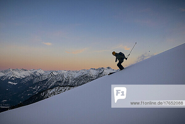 Mann fährt bei Sonnenuntergang auf einem schneebedeckten Berg Ski