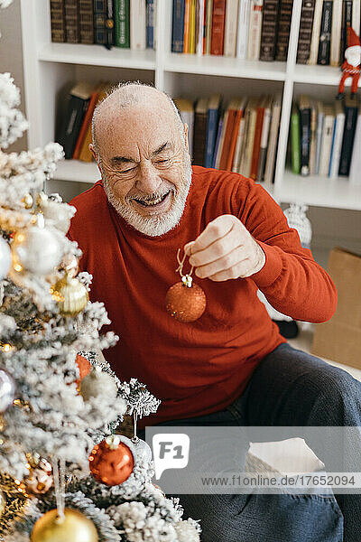 Glücklicher älterer Mann  der zu Hause den Weihnachtsbaum schmückt