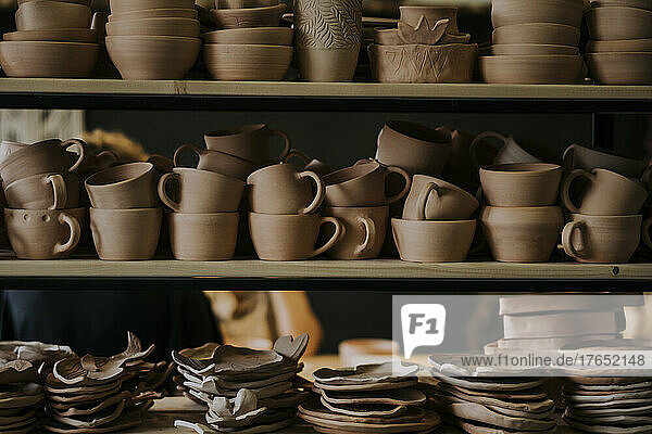 Handgefertigte Keramikschalen mit Tassen und Tellern auf dem Regal in der Werkstatt