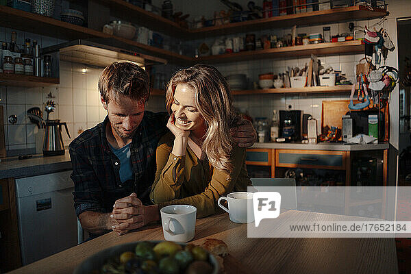 Couple holding hands sitting at dining table in kitchen