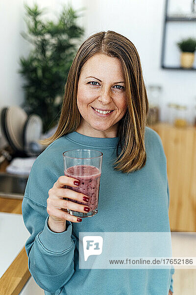 Smiling woman with glass of smoothie in kitchen at home
