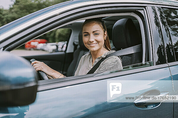 Lächelnde junge Frau  die durch das Autofenster schaut