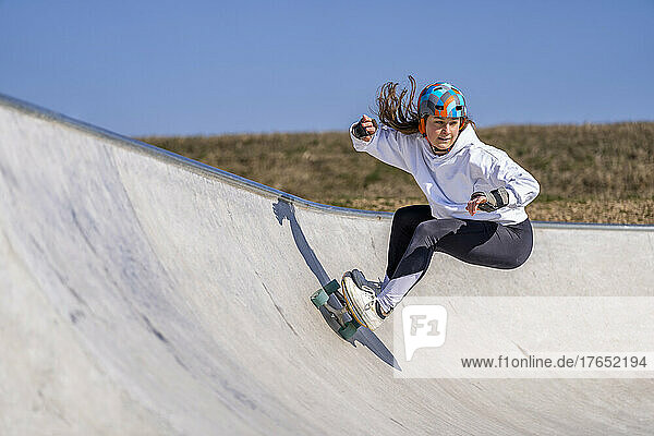 Young woman practicing skateboarding in pump track on sunny day