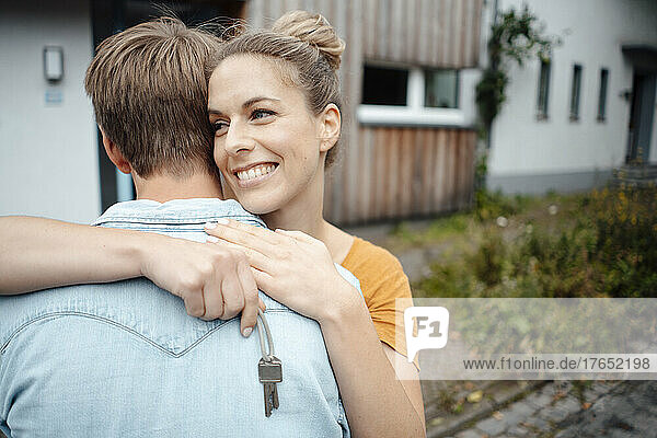 Happy blond woman holding house key hugging boyfriend at backyard