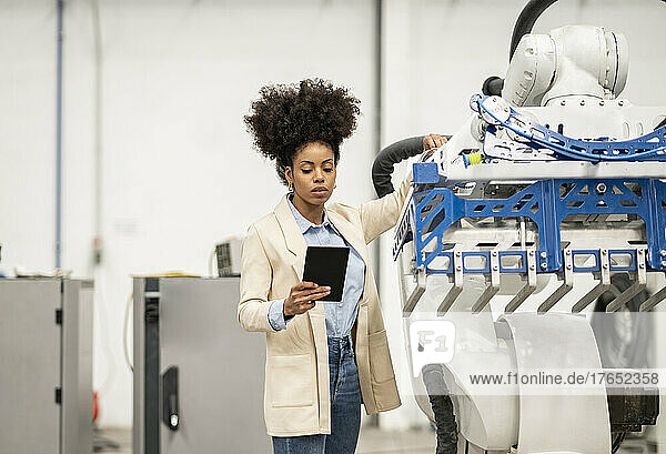 Businesswoman analyzing robotic arm through tablet PC in warehouse at factory