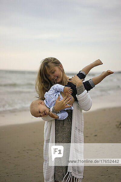 Happy mother carrying son on beach at sunset