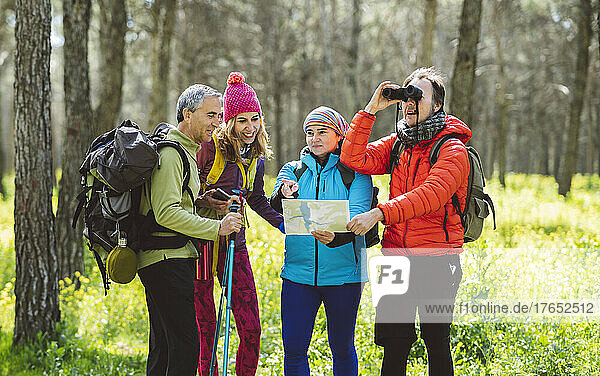 Mann schaut durch ein Fernglas und steht neben Freunden  die im Wald eine Karte teilen