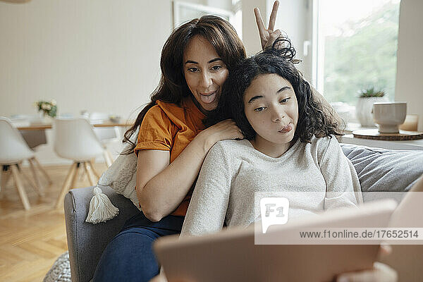 Frau und Tochter strecken die Zunge heraus und machen zu Hause ein Selfie mit dem Tablet-PC