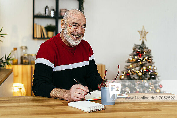 Glücklicher Mann mit Brille und Tagebuch zu Hause am Tisch