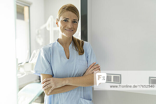 Smiling dentist standing with arms crossed in dental clinic