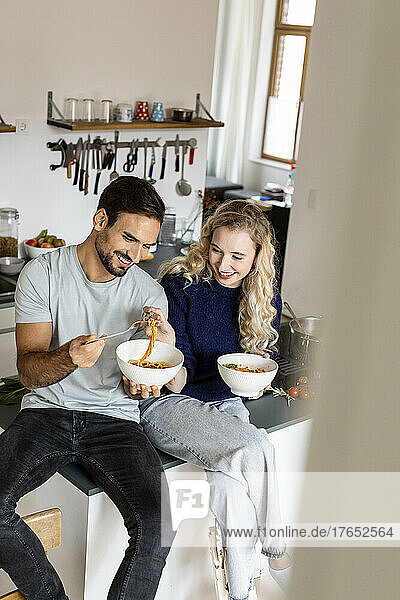 Smiling couple eating noodles in kitchen