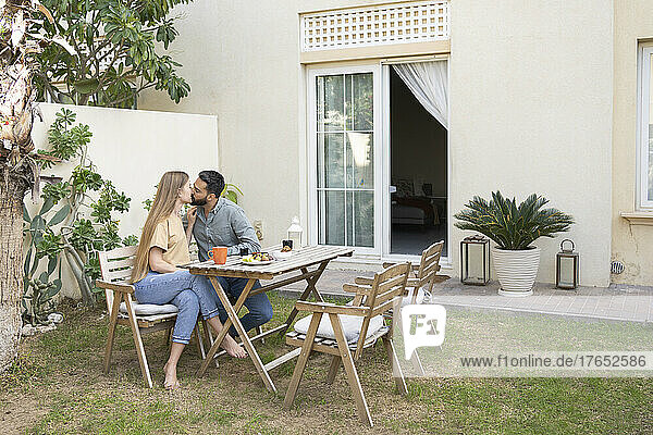 Couple sitting at table kissing each other in back yard