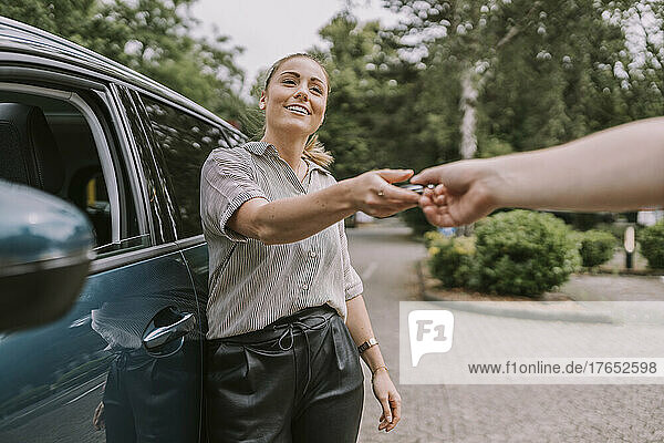 Smiling woman giving car key to man at parking lot