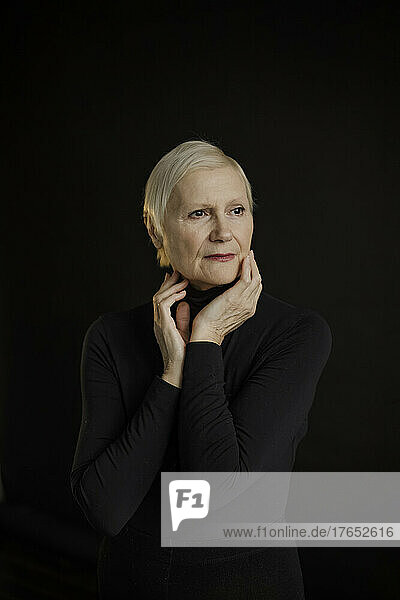 Thoughtful senior woman with short blond hair against black background