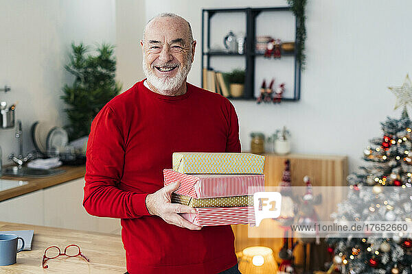 Glücklicher älterer Mann mit Geschenkboxen  der zu Hause am Tisch steht