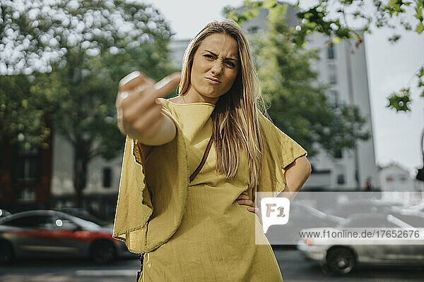 Angry woman doing obscene gesture standing on street