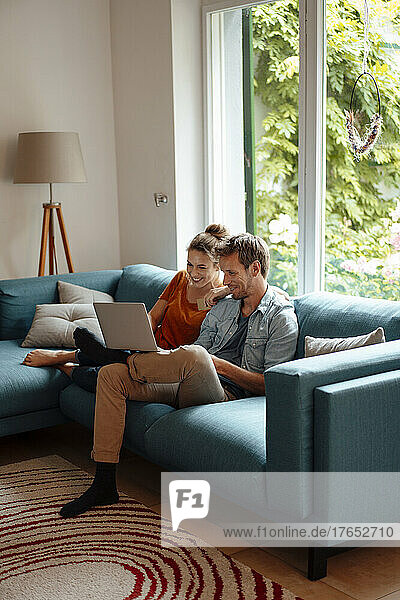 Happy couple sharing laptop sitting on sofa in living room at home