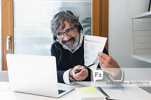 Smiling freelancer explaining document through video call on laptop at home
