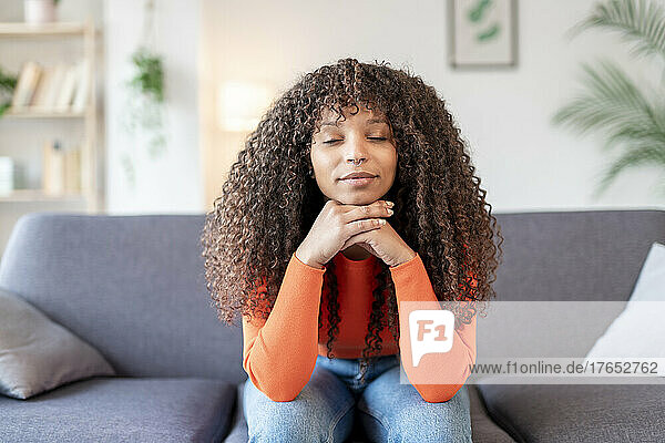 Young woman with eyes closed sitting on sofa at home