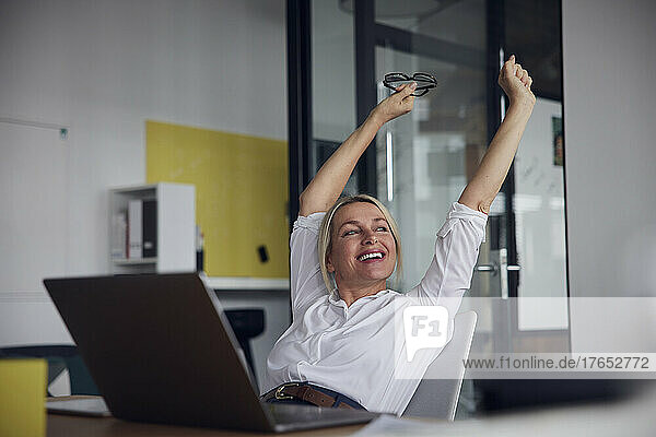 Happy businesswoman stretching with arms raised in office