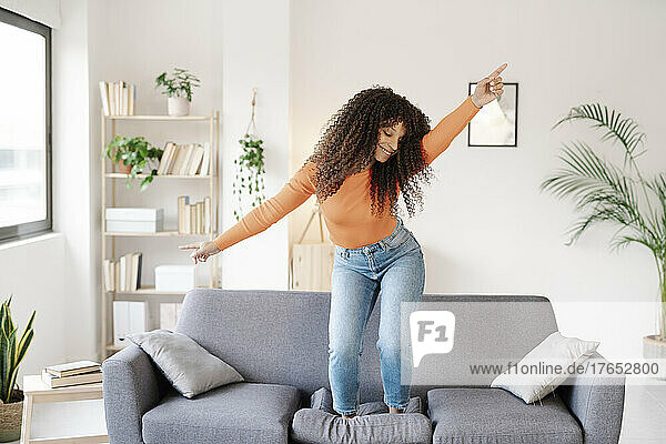 Smiling young woman dancing on sofa in living room at home