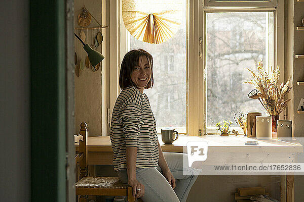 Happy woman sitting on chair by window at workshop