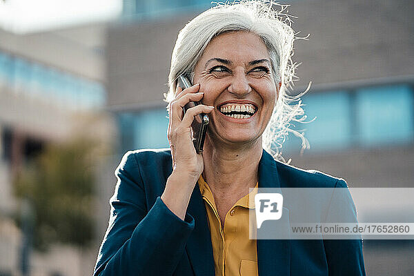 Cheerful businesswoman with gray hair talking on smart phone