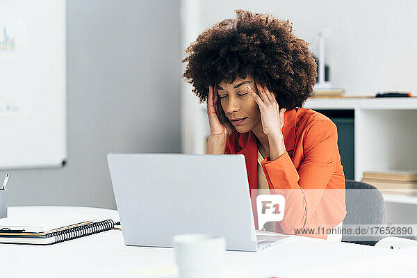 Businesswoman with head in hands sitting with laptop at desk in office