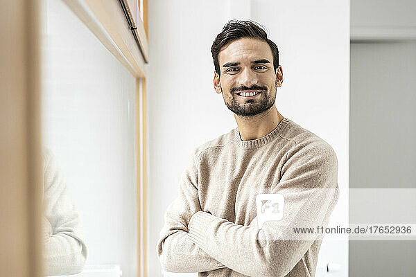 Smiling man with arms crossed near window at home
