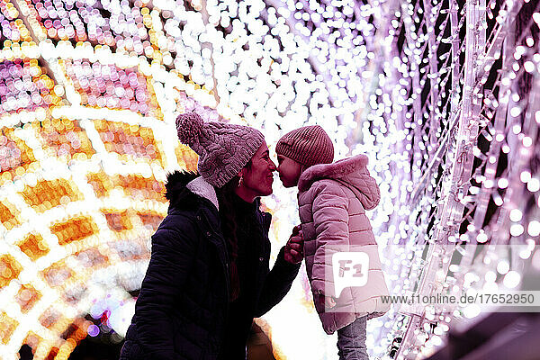Mother embracing cute daughter by Christmas lights