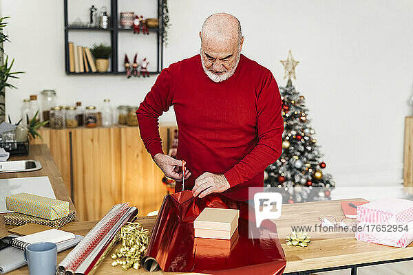 Senior man wrapping Christmas presents on table at home